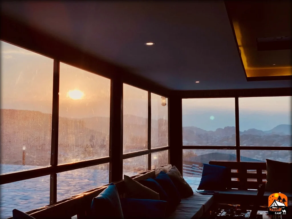 Camp lounge with floor-to-ceiling windows looking out over the mountains at sunset